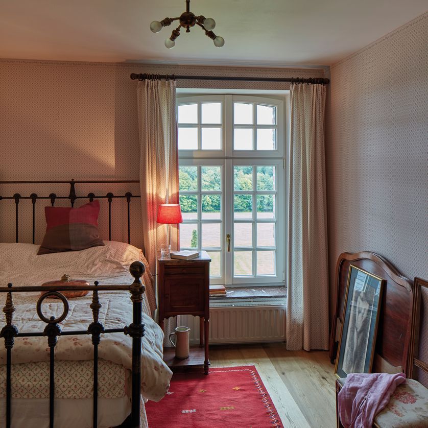 Grande fenêtre dans une chambre avec un lit sur la gauche.