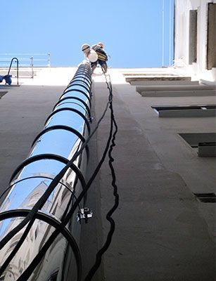Dos hombres están trepando por una tubería de metal en el costado de un edificio.