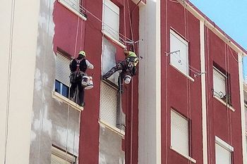 Dos hombres están pintando el costado de un edificio.