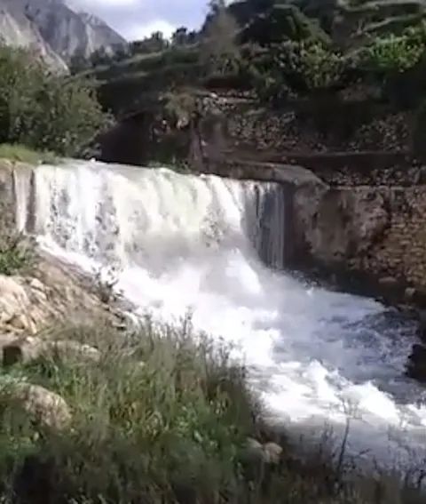 Una cascada en medio de un bosque con montañas al fondo.