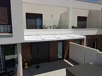 Exterior de un moderno apartamento de dos plantas con patio, balcón y toldo blanco sobre la planta baja.