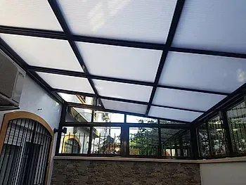 Patio exterior cubierto con paneles de techo translúcidos blancos y estructura de metal negro.