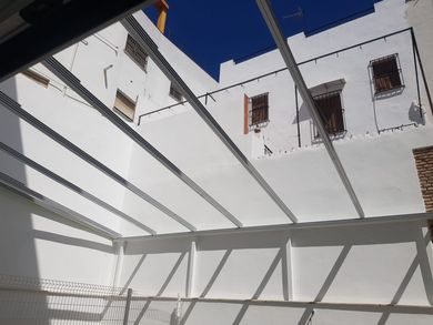 Patio blanco con vigas en el techo y cielo azul, rodeado de paredes blancas y ventanas con detalles de ladrillo.