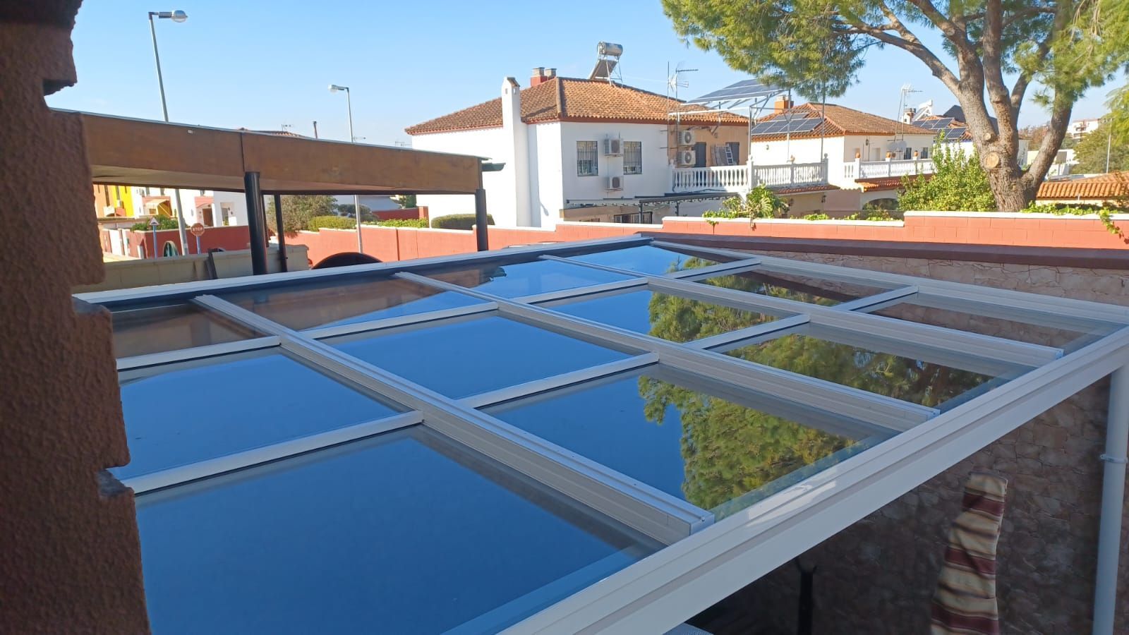 Paneles solares azules en un tejado con un edificio de ladrillos y árboles al fondo.
