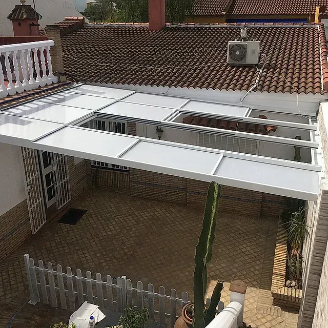 Patio con toldo retráctil blanco sobre un patio junto a una casa con tejas.