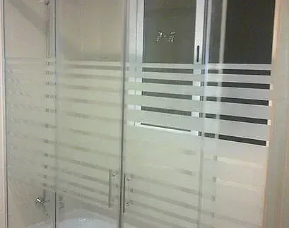 Mampara de ducha de cristal con franjas horizontales esmeriladas y tiradores metálicos.