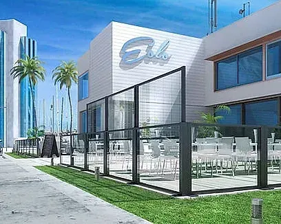 Exterior de edificio moderno con terraza al aire libre, valla de cristal, palmeras y detalles en azul.