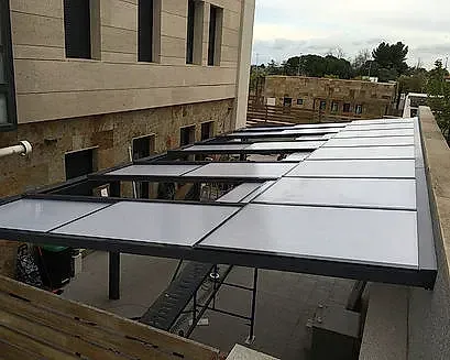 Pasarela exterior con estructura metálica y paneles de techo blancos junto a un edificio beige, en construcción.