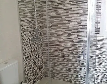 Baño con cabina de ducha alicatada y puerta corredera de cristal junto al inodoro.