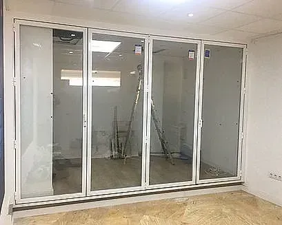 Grandes puertas corredizas de vidrio con marco blanco en una habitación luminosa y vacía con piso de baldosas e iluminación