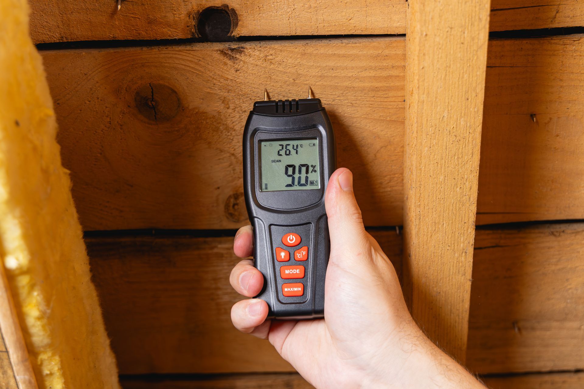 Une personne tenant un humidimètre numérique contre un montant mural en bois, affichant une lecture de 90 %