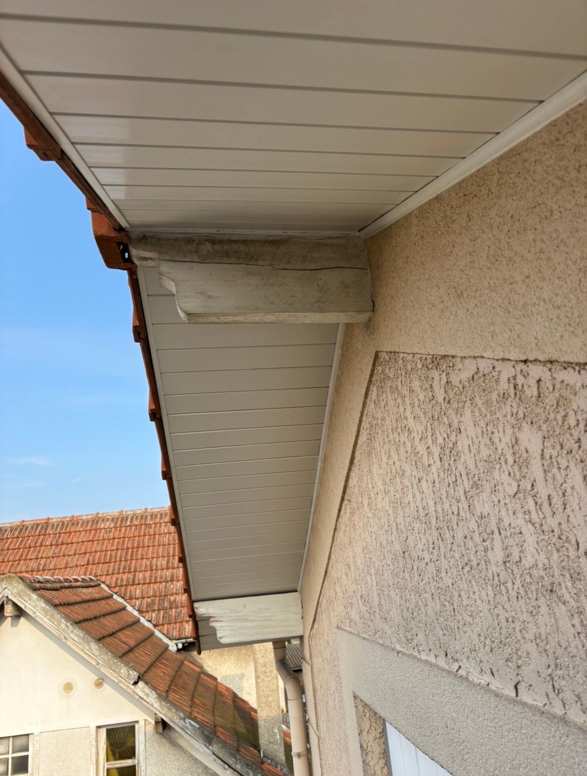 Gros plan sur un panneau de sous-toiture blanc sous l'avant-toit d'un bâtiment, montrant des chevrons en bois apparents