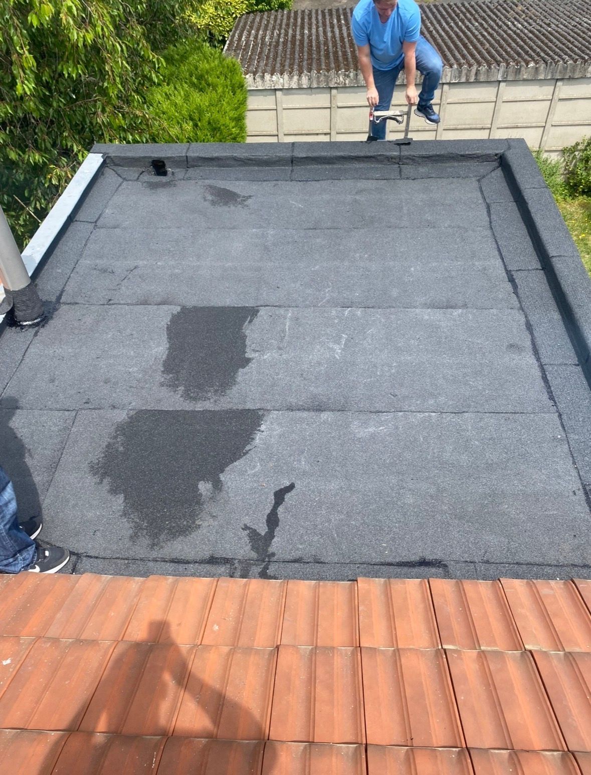Une personne travaille sur un toit plat en bitume gris foncé présentant des taches d'humidité