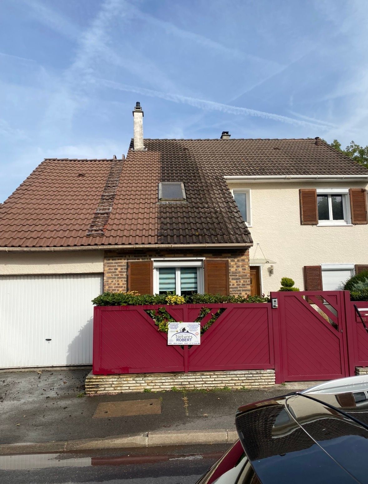 Une maison à un étage avec un toit de tuiles partiellement nettoyé, un garage blanc et une clôture bordeaux