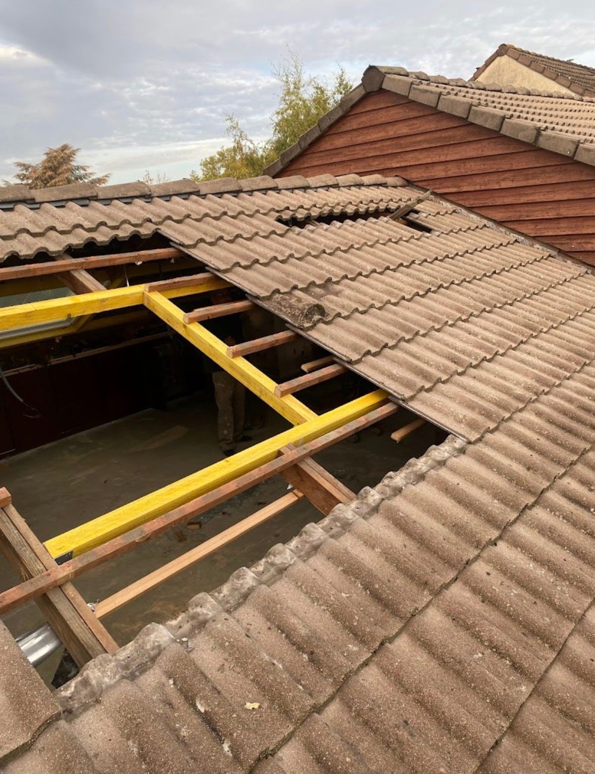 Toiture d'une maison partiellement déconstruite, laissant apparaître des poutres de soutien en acier jaune et des sections de tuiles