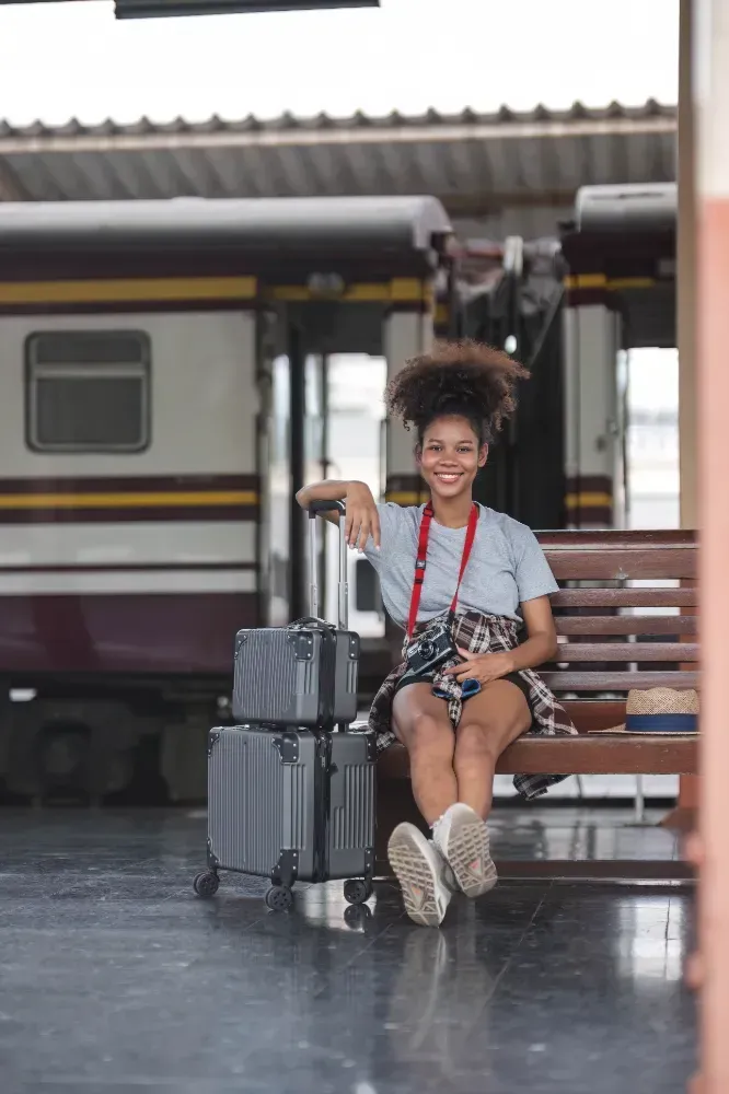 A woman is sitting on a bench at a train station with her luggage.