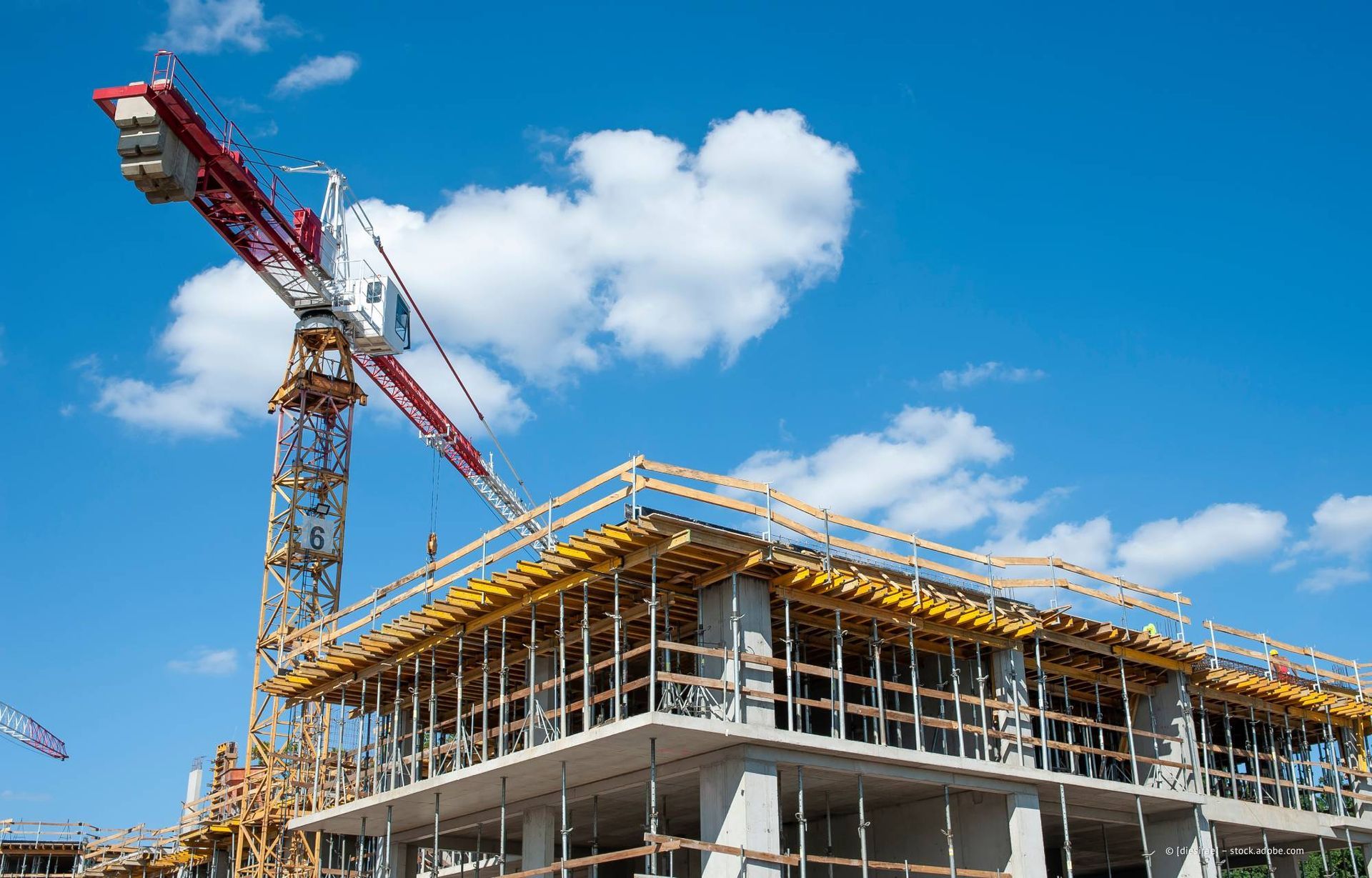 Baustelle mit einem Kran über einem Gebäuderahmen, blauem Himmel und Wolken.
