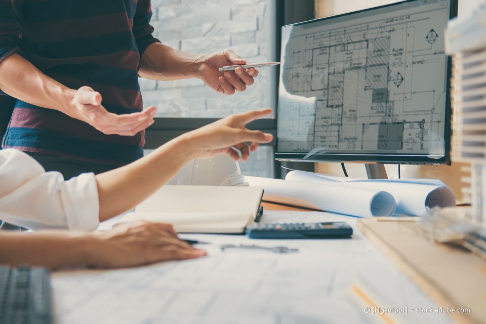 Architekten prüfen Gebäudepläne auf einem Computermonitor, zeigen und diskutieren den Entwurf.