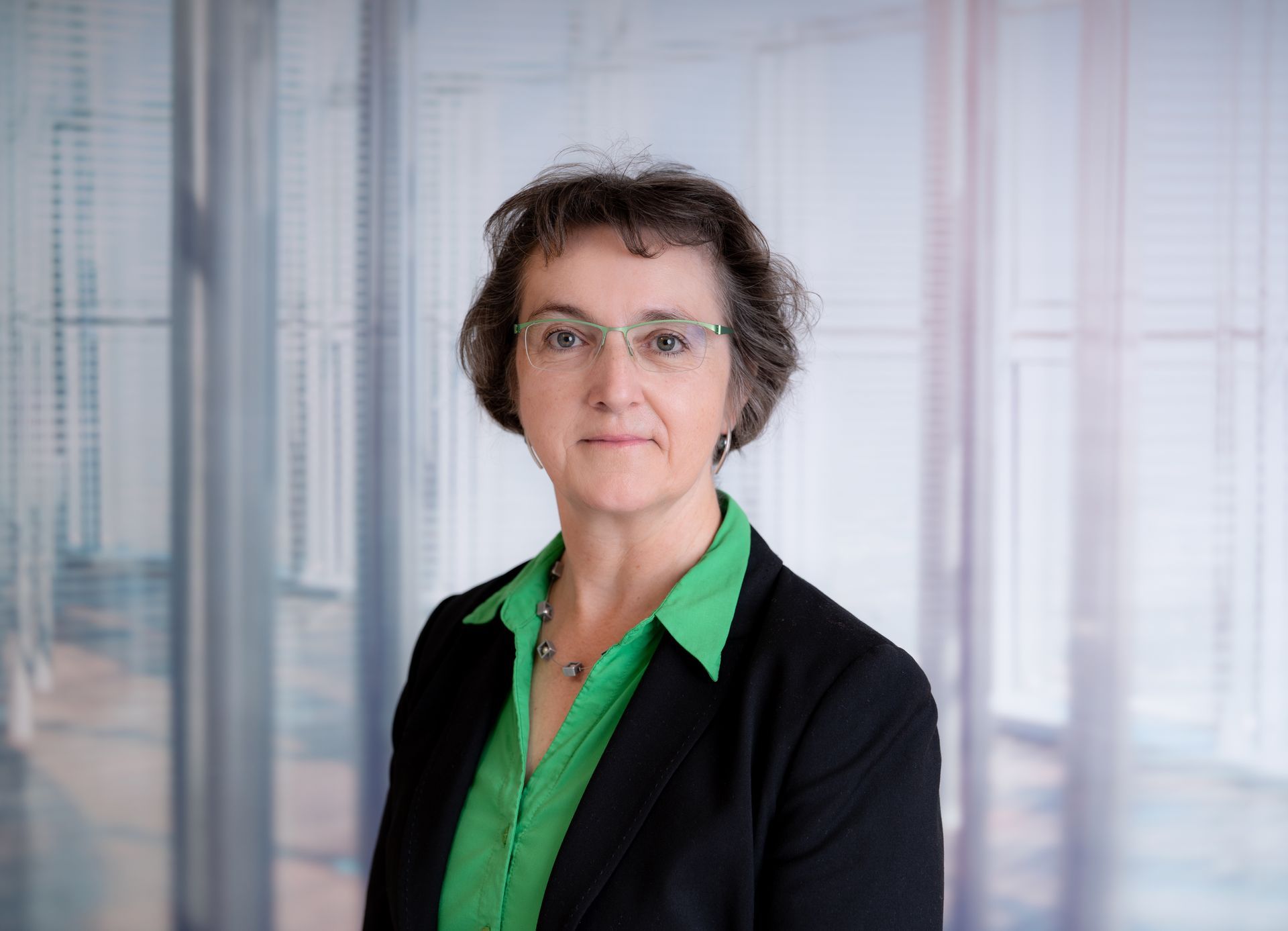 Frau mit Brille in grünem Hemd lächelt leicht vor einer Holztür.