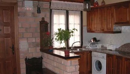 Cocina con muebles de madera, pared de ladrillo, ventana con cortinas y lavadora.