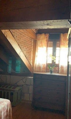 Dormitorio rústico abuhardillado con techo de madera inclinado, paredes de ladrillo, ventana y cómoda de madera.