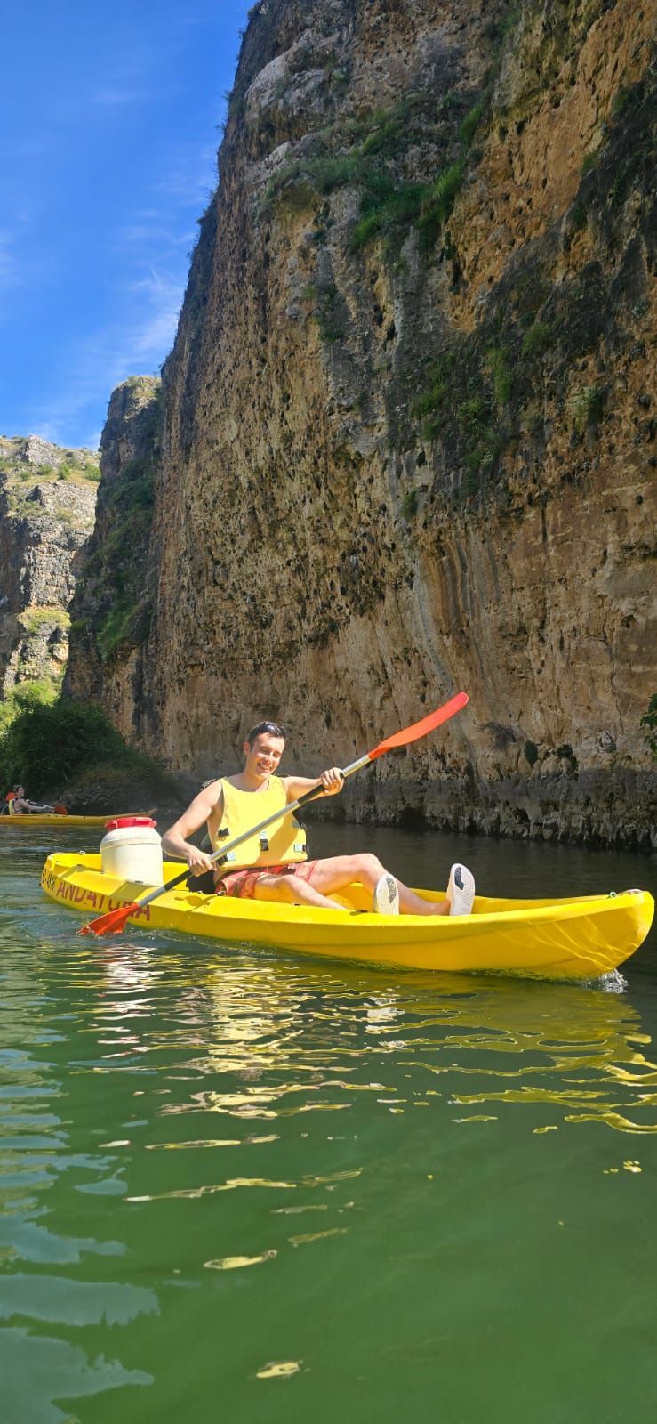 Una persona navegando en un kayak amarillo por un río junto a una gran formación rocosa.