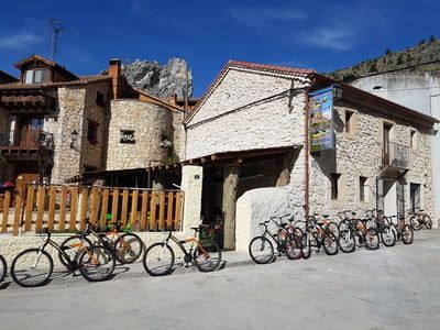 Fila de bicicletas estacionadas afuera de un edificio de piedra en un pueblo, con montañas como telón de fondo.