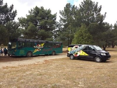 Autobús verde y camioneta negra estacionados en un camino de tierra, árboles al fondo.