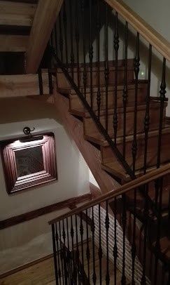 Escalera interior con barandilla de madera oscura y un espejo de pared enmarcado bajo un techo inclinado.