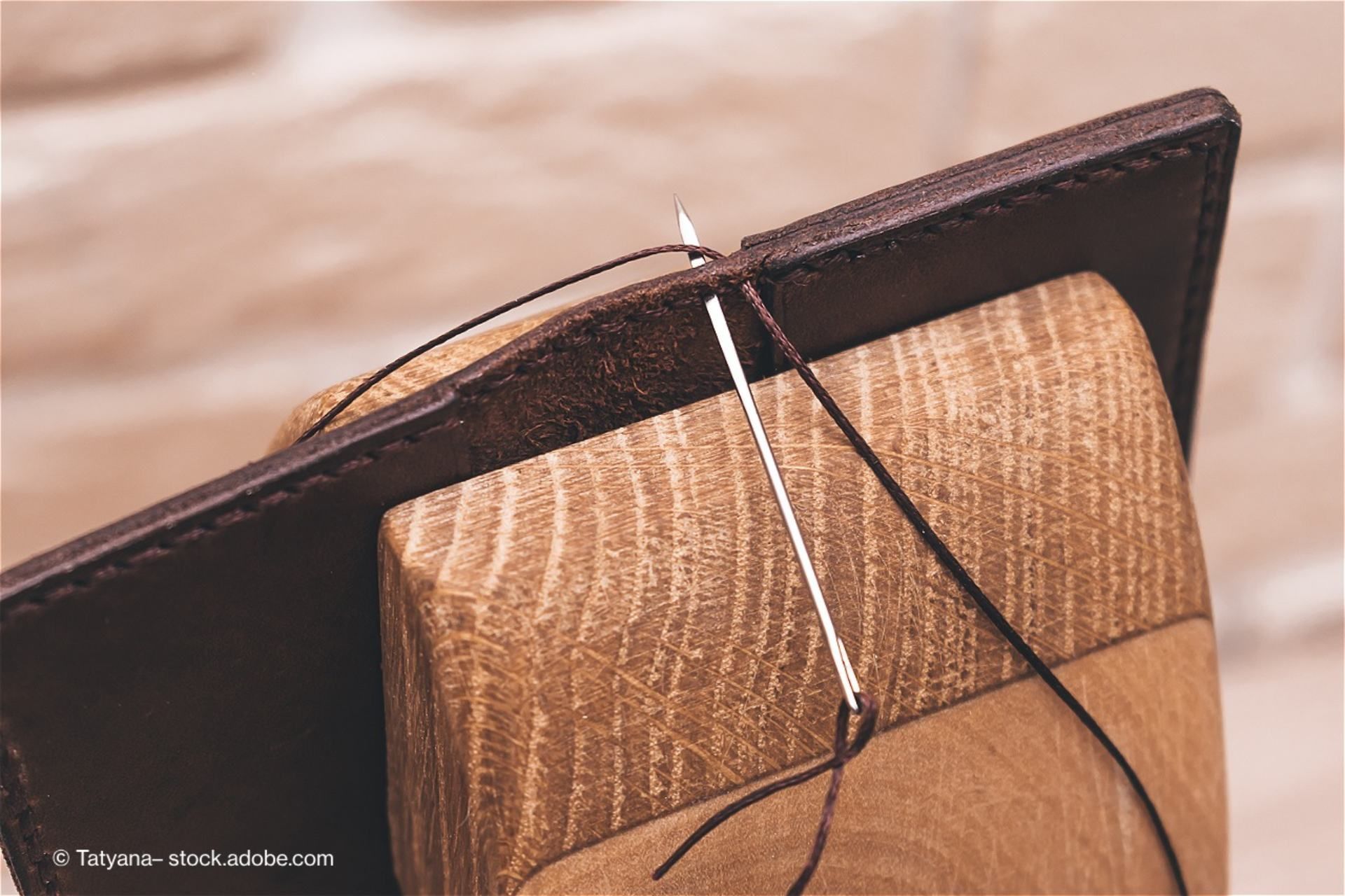 Eine Nadel mit einem Faden steckt in einem Stück Leder