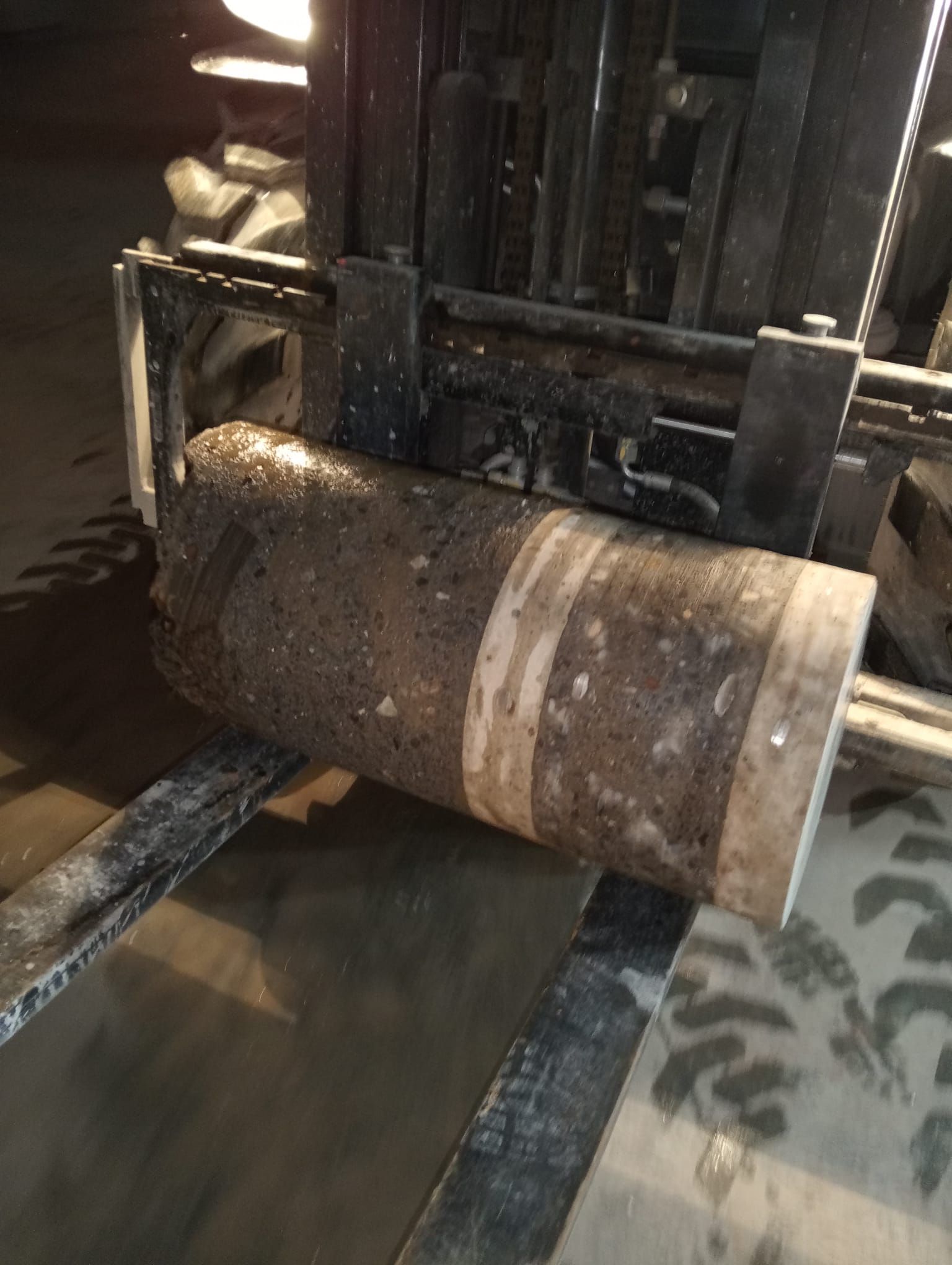 Tambor de metal oxidado sobre las horquillas de una carretilla elevadora en un entorno industrial con poca luz, con el suelo de hormigón mojado debajo.
