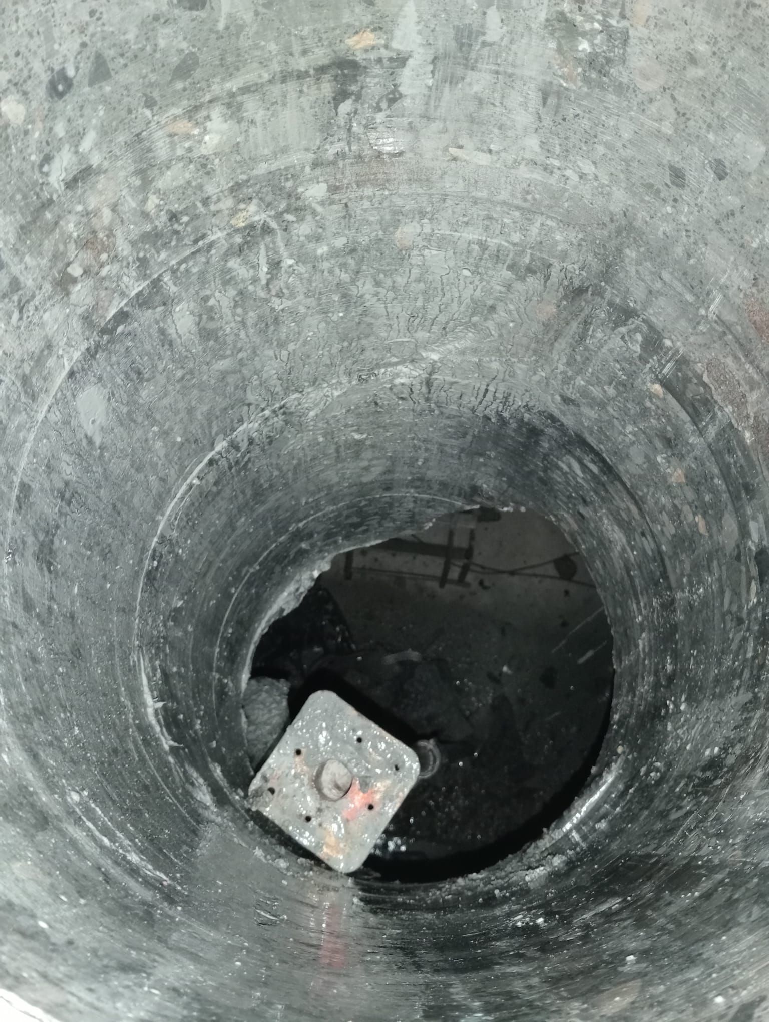 Mirando hacia abajo, se ve un profundo pozo de hormigón con una rejilla metálica en el fondo y una abertura oscura debajo.