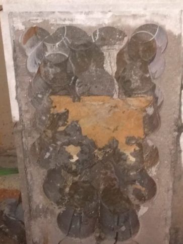 Panel eléctrico dañado con múltiples componentes redondos antiguos y pintura naranja descascarada en una pared.