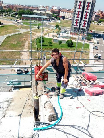 Un trabajador agachado en una azotea con herramientas, observando una calle de la ciudad.