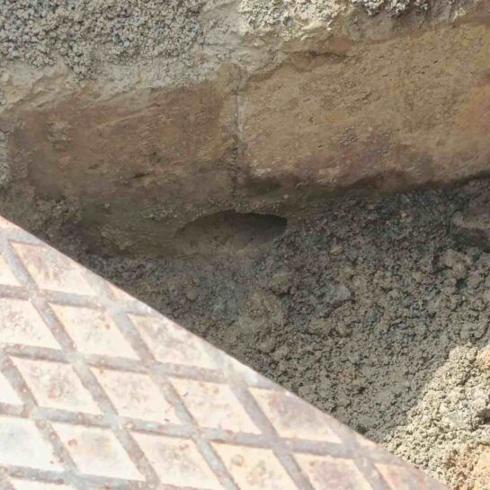 Primer plano de un muro de piedra tosca y grava junto al borde de un suelo de baldosas estampadas.