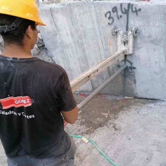 Un trabajador con casco utiliza una herramienta montada en la pared sobre una superficie de hormigón.