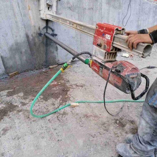 Un trabajador utiliza una sierra para cortar paredes con una manguera verde en una pared de hormigón en el interior.