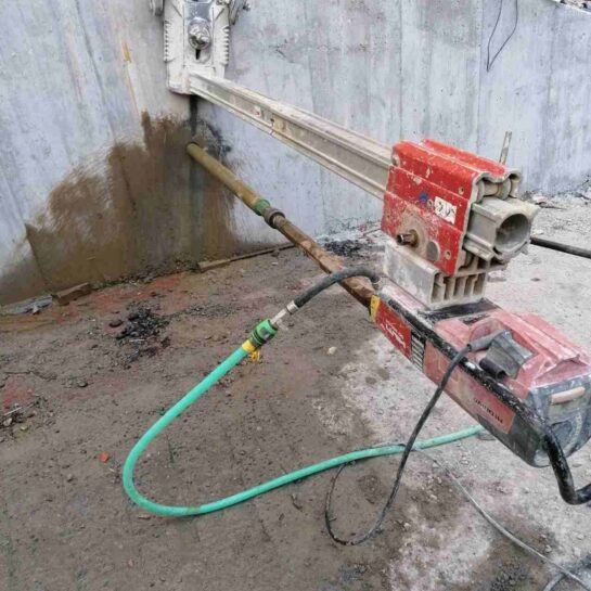 Bomba roja portátil y manguera verde en un rincón de hormigón del sótano con manchas de agua en la pared.