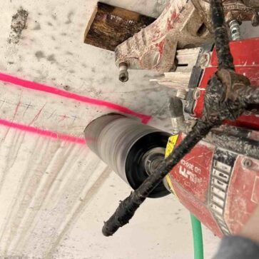 Un taladro de núcleo cortando un agujero en un techo de hormigón con líneas guía rosas marcadas cerca