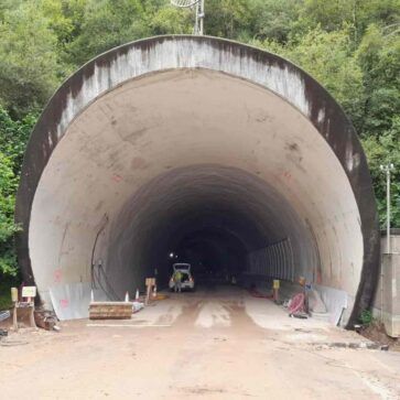 Entrada de un túnel de carretera con arco de hormigón, barreras de construcción y un vehículo en el interior.