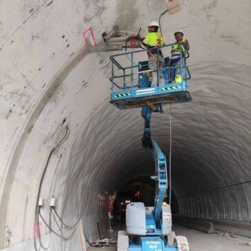 Trabajadores en una plataforma elevadora inspeccionando la pared curva de un túnel durante la construcción.