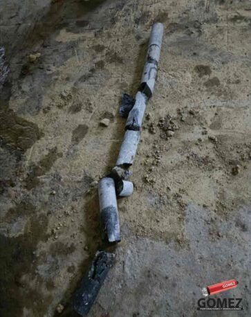 Trozos de tubería blanca rotos, tendidos sobre suelo fangoso y unidos por cinta adhesiva negra.