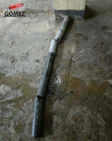 Tubería negra rota con un conector de PVC blanco, tirada sobre un suelo de hormigón mojado.