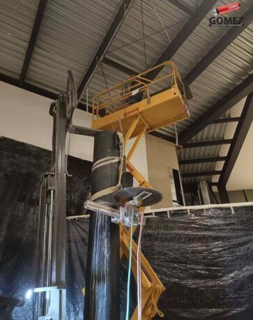 Plataforma de trabajo elevada de color amarillo junto a una gran tubería negra en un almacén industrial.