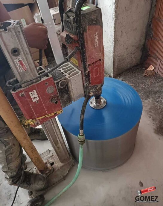 Máquina perforadora conectada a un tanque de agua azul y gris en un área de trabajo.