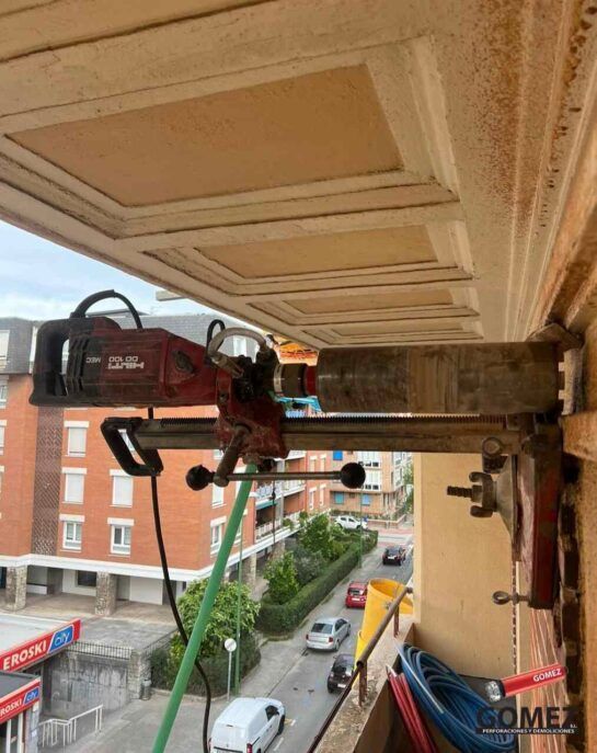 Un trabajador, subido a una plataforma elevadora, repara el techo ornamentado de un edificio en una calle con vistas.