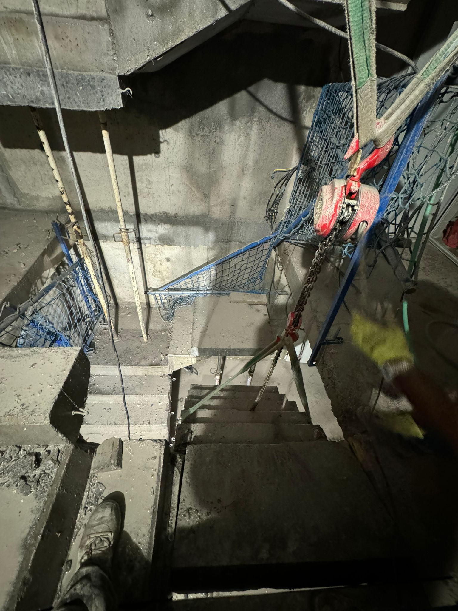 Escalera en construcción con escalones de hormigón, red de seguridad azul y cuerdas rojas en la parte superior.