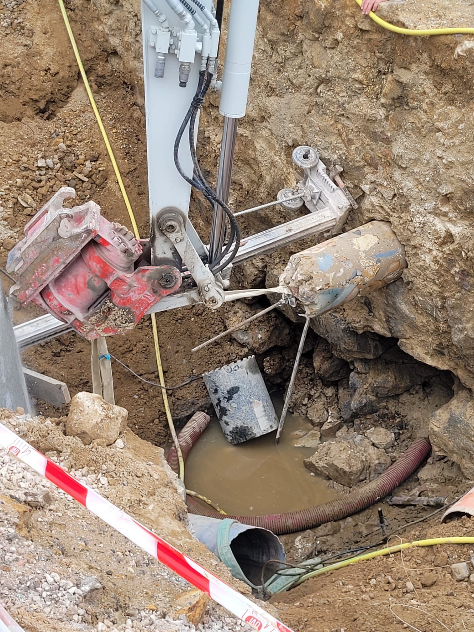 Zanja de servicios públicos con tuberías, cables y equipos dañados expuestos en un sitio de excavación de tierra.