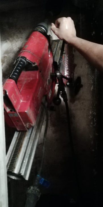 Persona sosteniendo una herramienta eléctrica roja contra una superficie de metal oscuro en un espacio de trabajo .