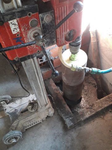 Máquina industrial llenando una botella con líquido verde junto a un tubo transparente en el suelo de un taller.